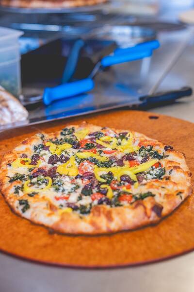 An Athenian pizza with spinach, olives and yellow peppers on a round board by the pizza cutters