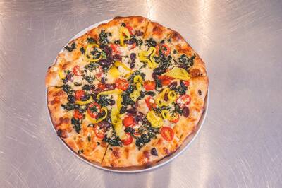 An Athenian pizza with spinach, kalamata olives, tomatoes and yellow hot peppers, seen from above