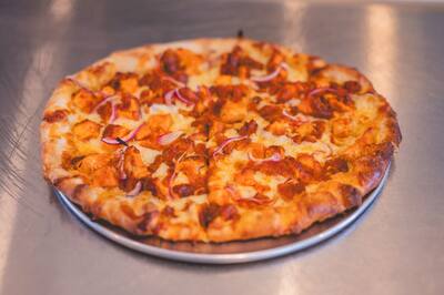 A Buffalo Chicken pizza with red onion on a round tray