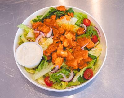 A Buffalo Chicken salad with crispy buffalo chicken, romaine, tomato, red onion and a cup of blue cheese, seen from above