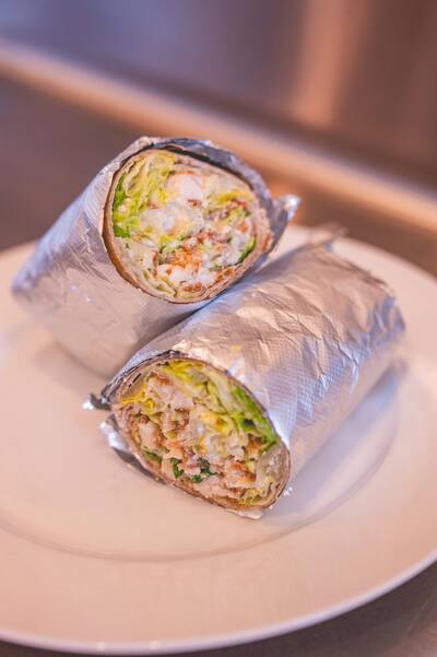 Two chicken Caesar wraps cut in half and wrapped in foil, on a white plate