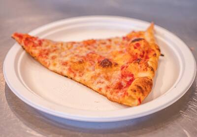 A cheese slice on a white paper plate, from the side