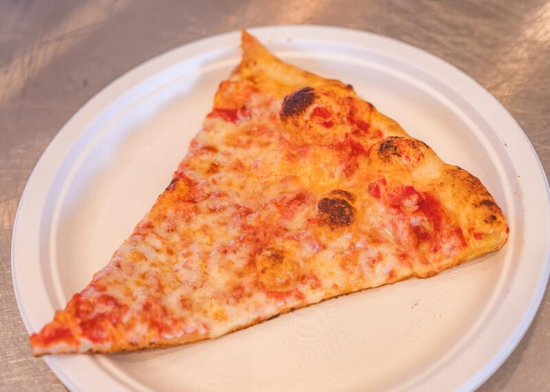 A big triangle cheese slice on a white paper plate