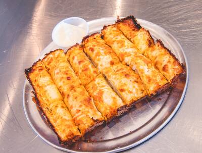 A pan of cheesy bread cut into sticks with a cup of dip