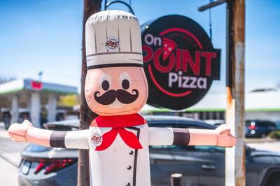 The inflatable chef out front with arms wide beside the On Point Pizza sign