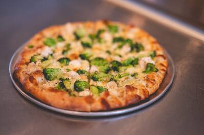 A Chicken and Broccoli pizza, a white pizza with chicken and broccoli, from the side