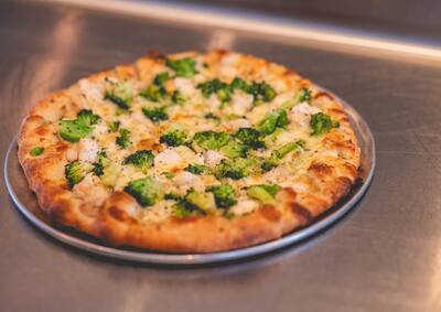 A Chicken and Broccoli pizza, a white pizza with chicken and broccoli, three quarter view