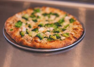 A Chicken and Broccoli pizza, a white pizza with chicken and broccoli, on a round tray