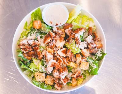 A chicken Caesar salad with croutons and a cup of dressing