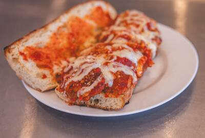 A Chicken Parm grinder, open, with marinara and melted cheese on a white plate
