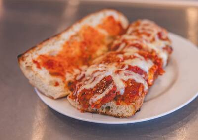 A Chicken Parm grinder with marinara and melted cheese, close to the camera