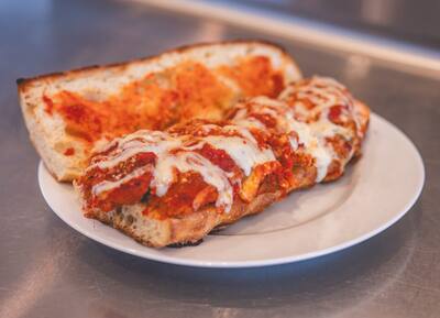 A Chicken Parm grinder with marinara and melted cheese on a white plate, from the side