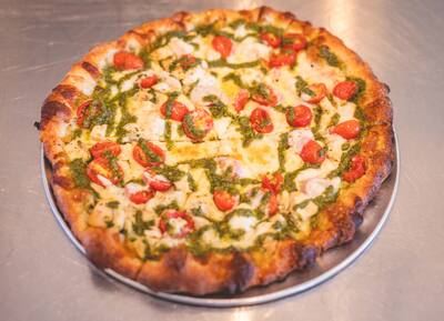A Chicken Pesto pizza with lines of pesto, fresh mozzarella and cherry tomatoes