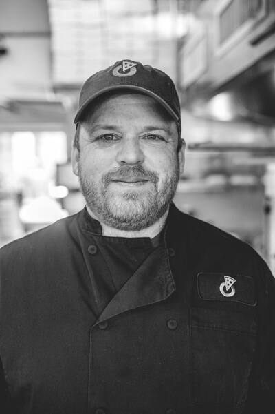 A black and white portrait of a cook in a cap and chef coat