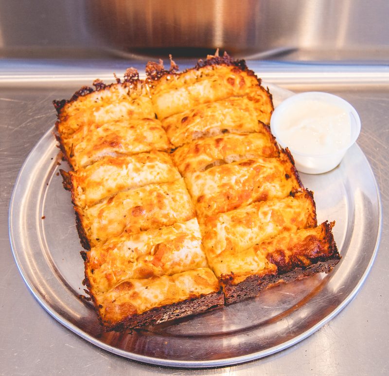 A Detroit style cheese pizza with a cup of ranch