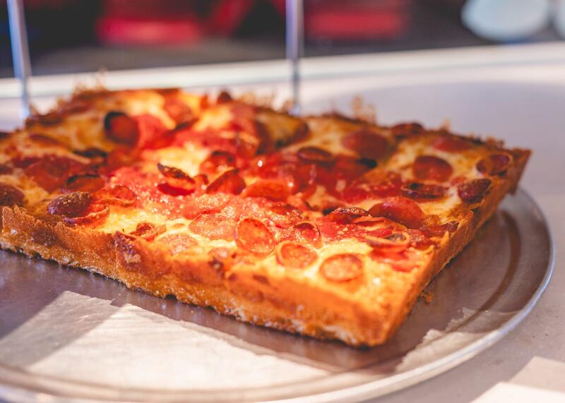 A Detroit style pepperoni pizza on a round tray, close to the camera