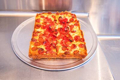 A Detroit style pepperoni pizza on a round tray on a steel counter
