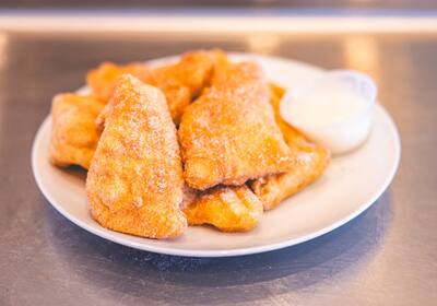Cinnamon sugar dough boys on a white plate with a cup of white dip, close up