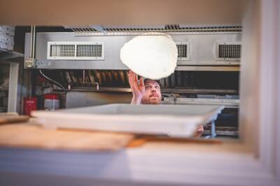 Pizza dough high in the air above a tray of dough in the kitchen