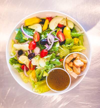 A garden salad with olives, peppers and tomatoes and a cup of dressing