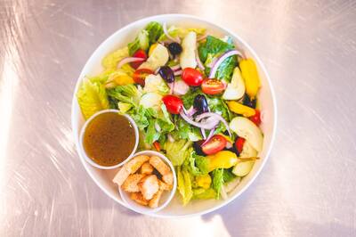 A garden salad with olives, tomatoes, banana peppers and croutons, with a cup of dressing