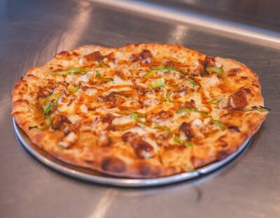 A General Tso's pizza with crispy chicken, green peppers and a sweet and spicy sauce on a round tray