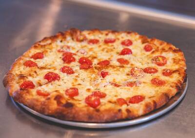 A Greek pizza with tomatoes and herbs over melted cheese, with no red sauce, on a round tray