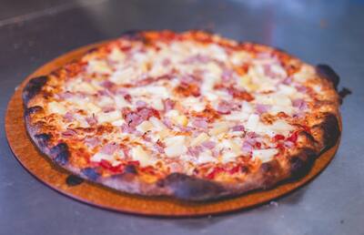 A Hawaiian pizza with ham and pineapple on a round board