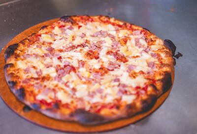 A Hawaiian pizza with ham and pineapple on a round board, from another angle