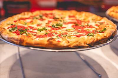 A margherita pizza with fresh basil on a stand in the slice case