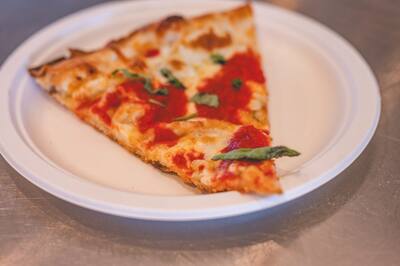 A slice of margherita pizza with fresh basil on a paper plate