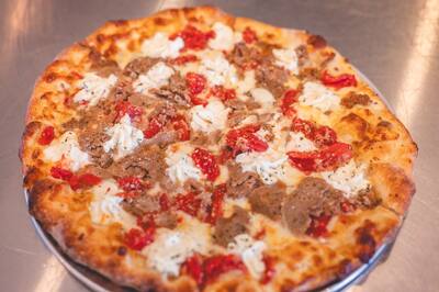 A Meatball Parm pizza with crumbled meatball, Roma tomato and ricotta, close to the camera