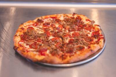 A Meatlovers pizza with pepperoni and crumbled sausage on a steel counter, from the side