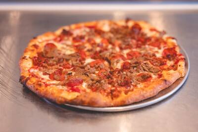 A Meatlovers pizza with pepperoni and crumbled sausage on a steel counter