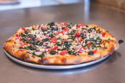 A Mediterranean pizza with spinach, black olives, tomatoes and feta on a round tray, from the front