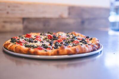 A Mediterranean pizza with spinach, black olives and tomato shot low across the steel counter