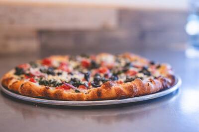 A low angle look at a Mediterranean pizza with spinach, black olives and tomatoes on a steel counter