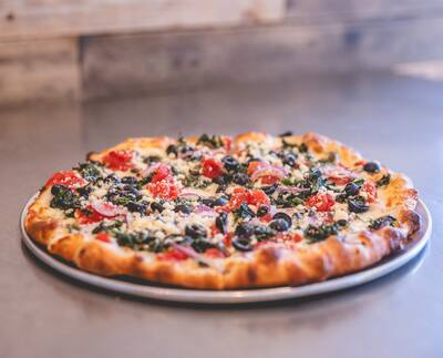 A Mediterranean pizza with spinach, black olives, tomatoes and feta on a round tray, from a low angle
