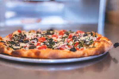 A Mediterranean pizza with spinach, black olives, tomatoes and feta on a round tray, from the side