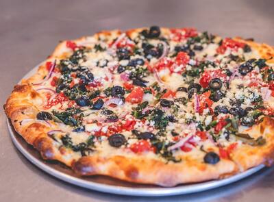 A Mediterranean pizza with spinach, black olives, tomatoes and feta on a round tray, three quarter view