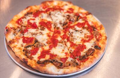 A Moussaka pizza with spoonfuls of marinara over melted cheese on a round tray