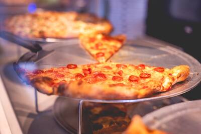 A pepperoni pizza and a slice on a stand in the slice case