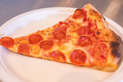 A pepperoni slice on a white paper plate, close up
