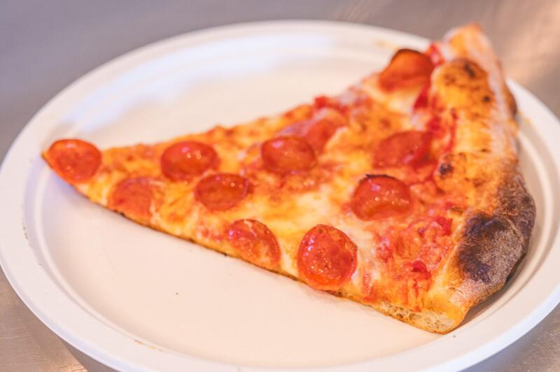 A pepperoni slice with a browned crust on a white paper plate