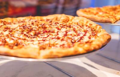 A round pizza with a drizzle of sauce on a stand in the slice case