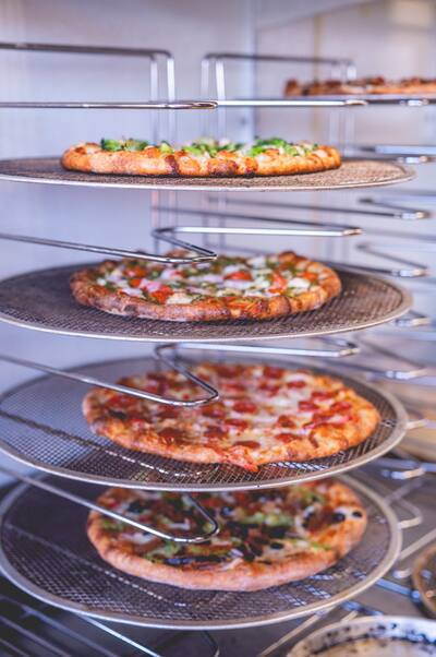Pizzas with broccoli, tomato and pepperoni on a tiered wire rack, from another angle