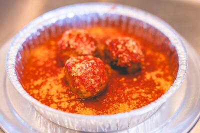 Three meatballs in red sauce with grated cheese in a foil tin