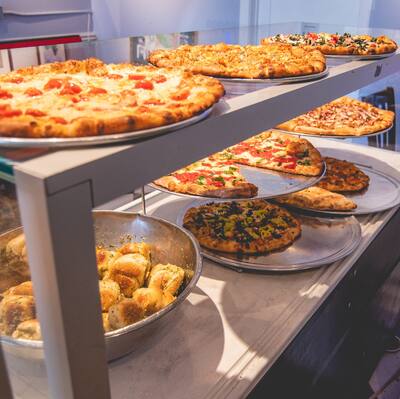 Whole pies and a bowl of garlic knots in the slice case