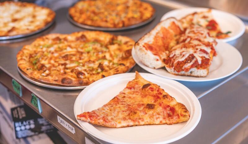 A cheese slice, a sandwich and whole pizzas set out together on the counter