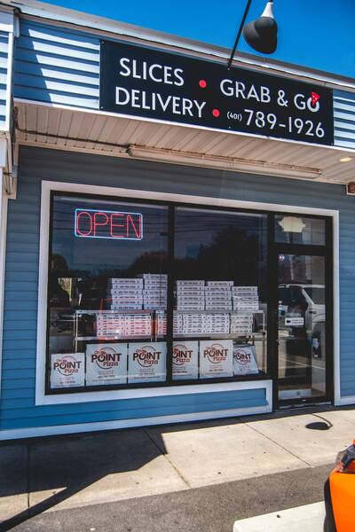 The storefront with the slices, grab and go and delivery sign and an open sign in the window
